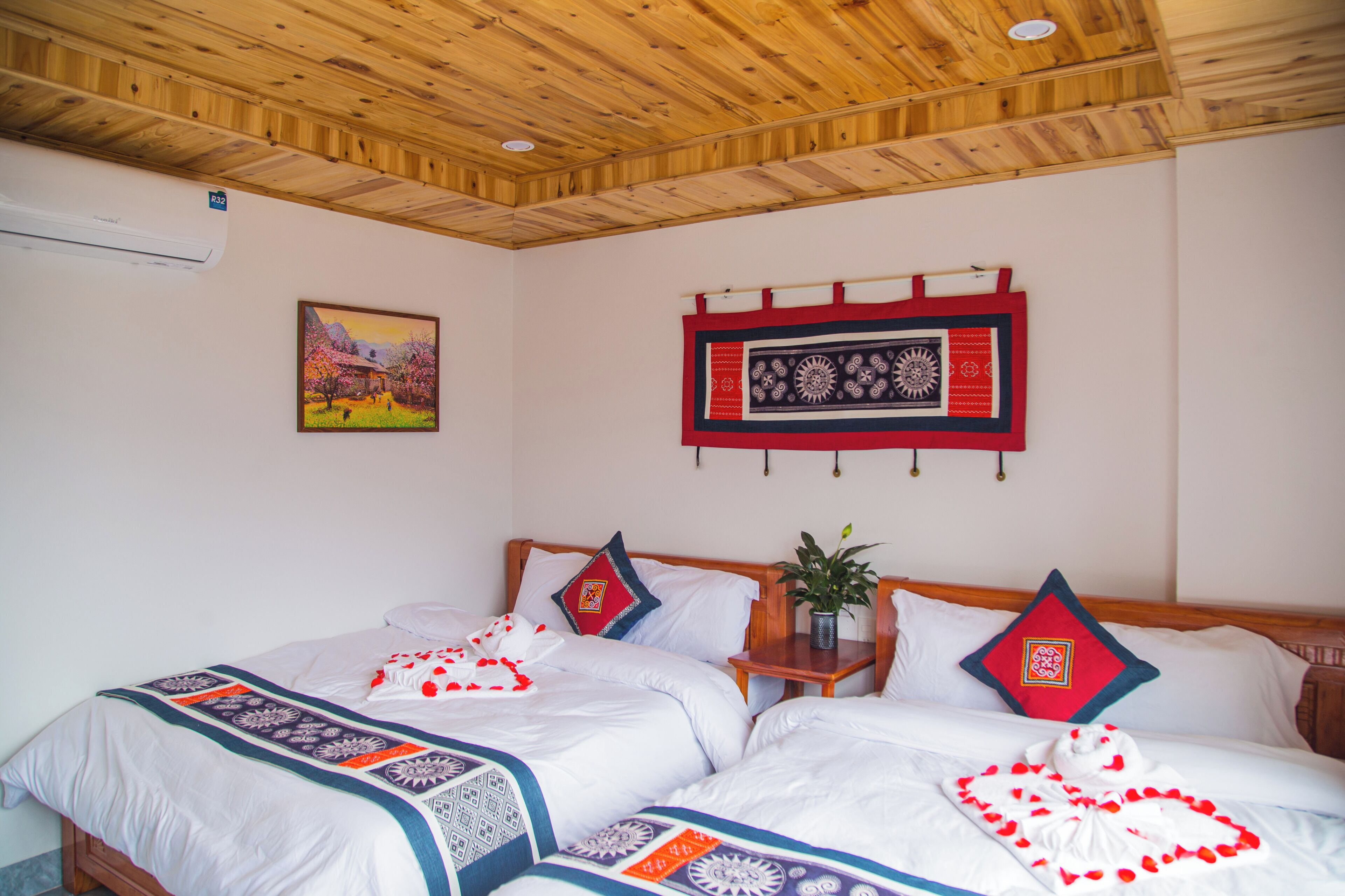 A hotel room with two beds, a wooden ceiling, a painting, and a decorative wall hanging.