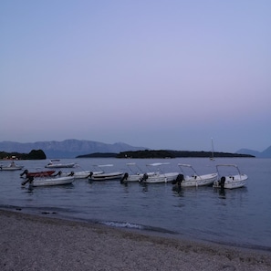 A row of boats docked at a calm body of water with a mountainous backdrop. - Three Island View Hotel (Lefkada)