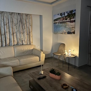 A living room with a sofa, a chair, a coffee table, a small table with a lamp, and a wall-mounted picture. - Three Island View Hotel (Lefkada)