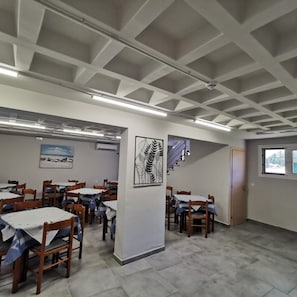A dining area with tables and chairs, a staircase, and artwork on the walls. - Three Island View Hotel (Lefkada)