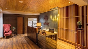 A reception area with a wooden reception desk, a red chair, and a wall-mounted sign. - Udaan Alpine Resort & Chongeytar (Gangtok)