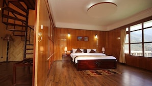 A bedroom with a wooden floor, a bed with pillows, a nightstand, a lamp, and a window with a view. - Udaan Alpine Resort & Chongeytar (Gangtok)