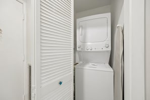 A compact laundry room with a built-in washer and dryer, a door with a star-shaped lock, and a window with horizontal blinds. - Updated 2BR - Omni villa - Near beach (Fernandina Beach)