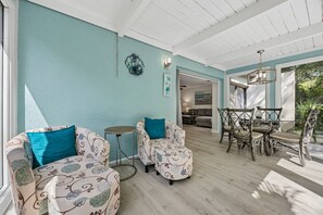 Ein Zimmer mit hellblauer Wand, Holzboden, einer Essecke mit Tisch und Stühlen sowie einem Sofa mit gemusterten Kissen.