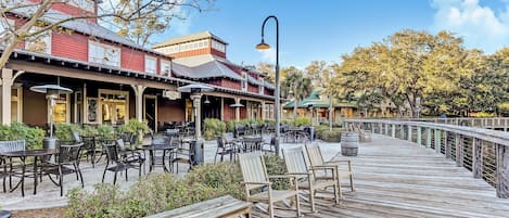 A wooden deck with outdoor seating, a covered patio area, and a building with a red facade.