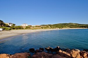 Un paisaje costero con una playa arenosa, agua tranquila y afloramientos rocosos.