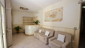 A living room with a sofa set, a small cabinet, a potted plant, and a map on the wall. - Il Gabbiano Hotel (Trinità d'Agultu e Vignola)