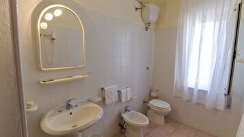 A bathroom with a sink, bidet, toilet, and a mirror with lights.