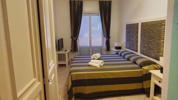 A hotel room with a bed, a desk, a television, and a window with curtains. - Il Gabbiano Hotel (Trinità d'Agultu e Vignola)