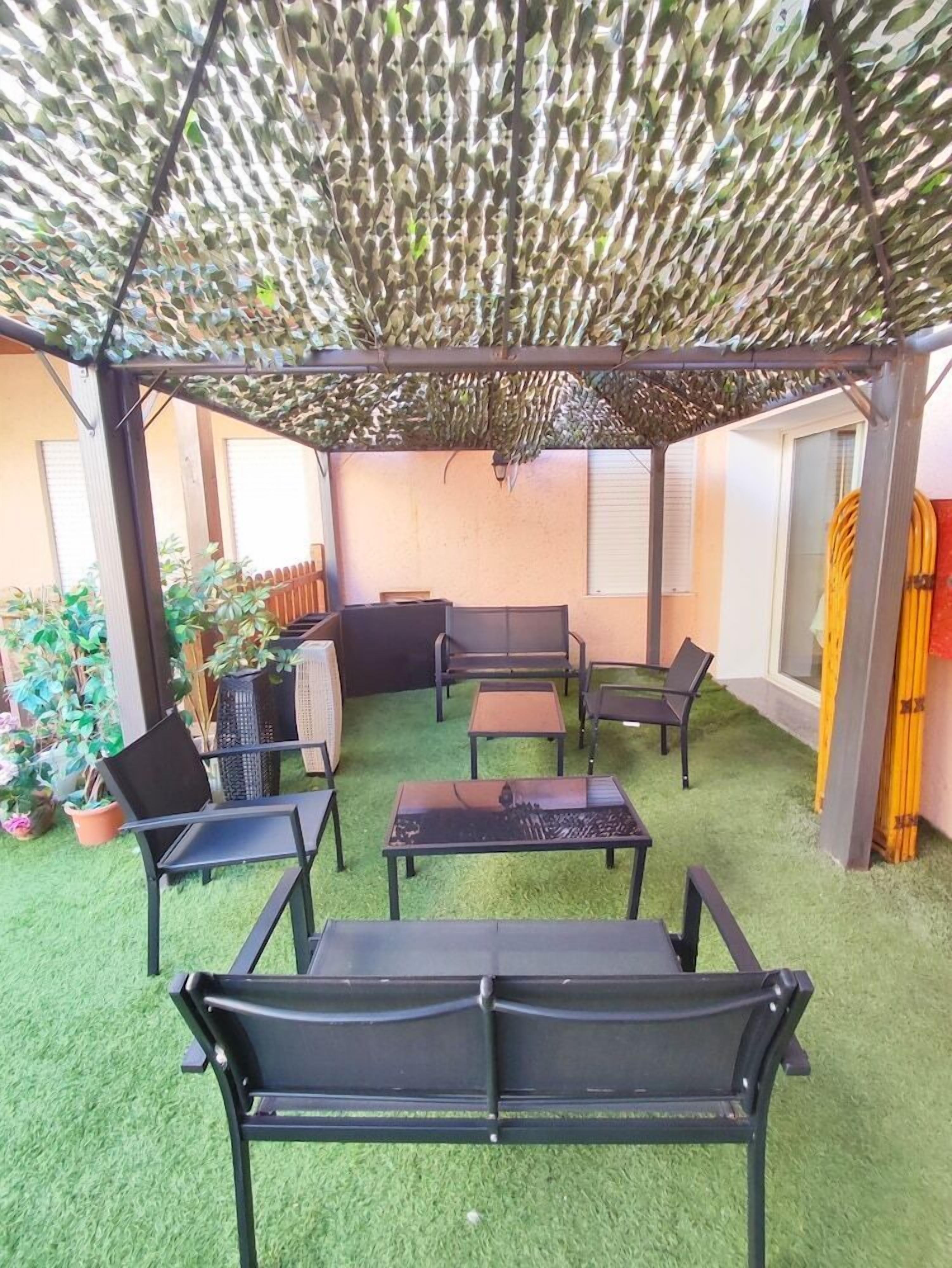 Un'area patio esterna con una pergola, prato sintetico verde e mobili in metallo nero.