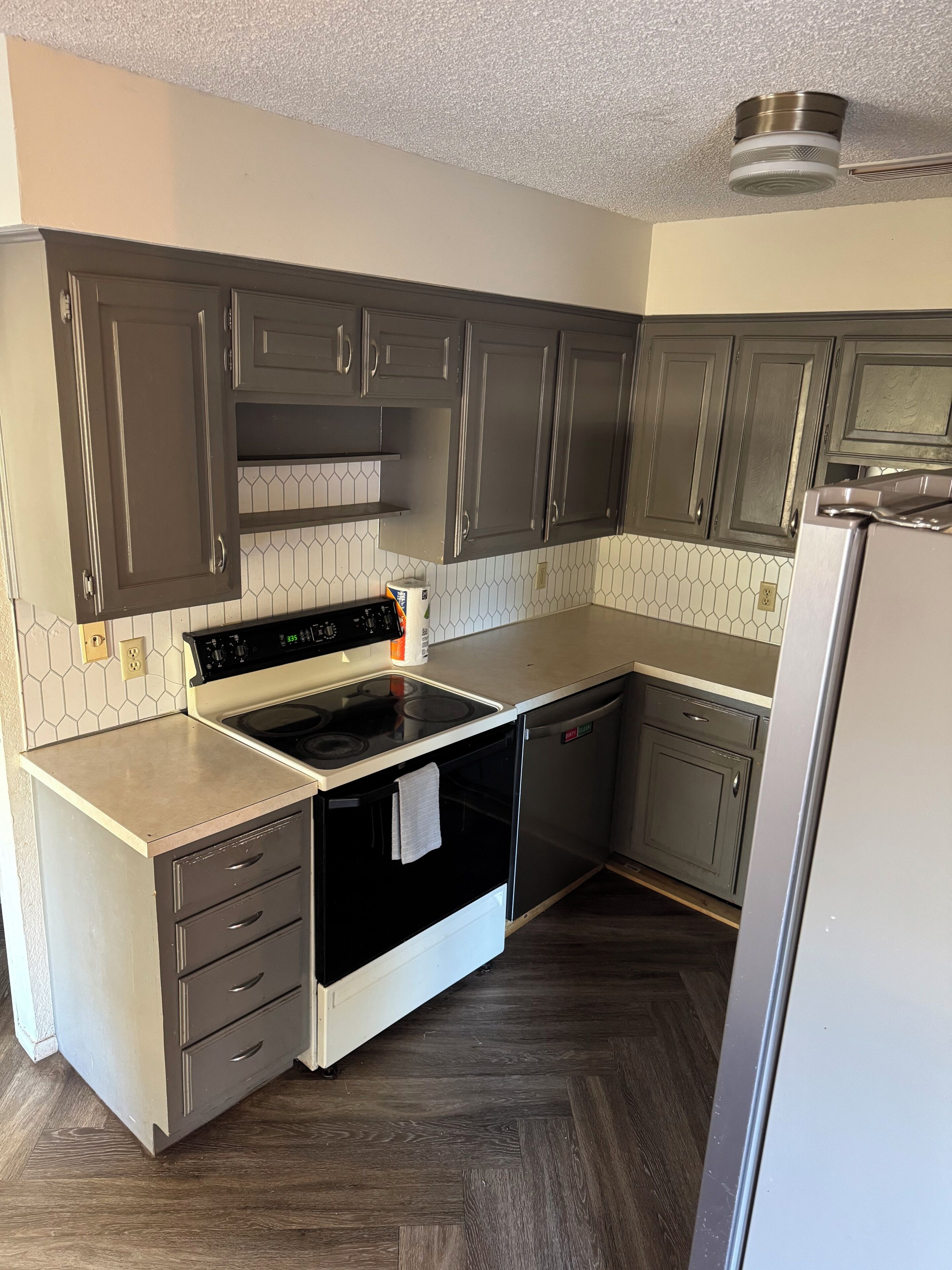 A kitchen with dark cabinets, a white countertop, a stove, a dishwasher, and a refrigerator.