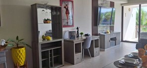 Cozinha moderna com eletrodomésticos embutidos, sala de jantar com mesa posta para quatro e uma grande janela com vista para palmeiras.