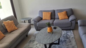 Un salon avec un canapé gris, deux petites tables d’appoint et une table basse ronde sur laquelle est posée une plante.