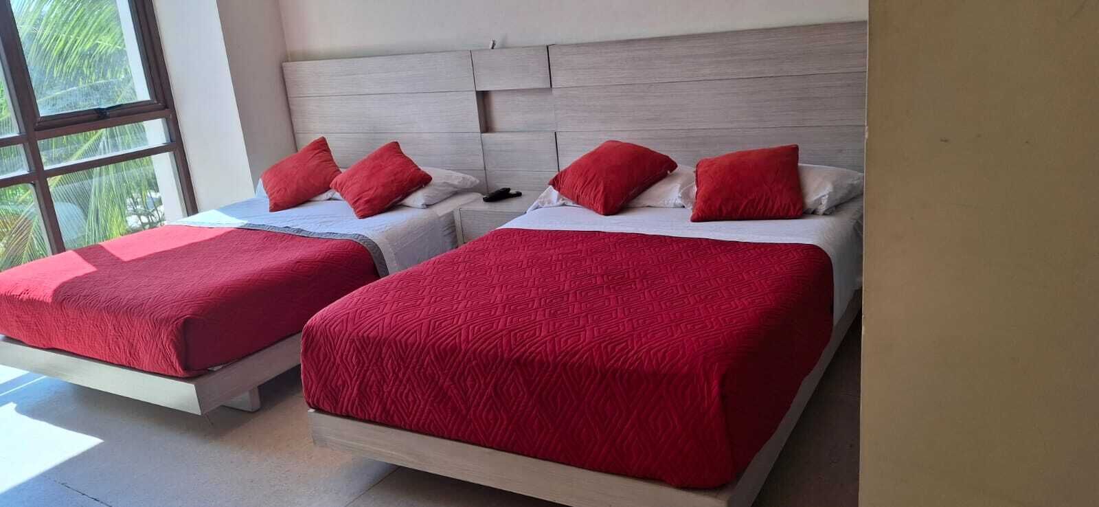 Zwei Betten mit roter Bettwäsche und ein heller Kopfteil in einem Zimmer mit einem großen Fenster.