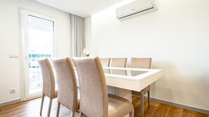 A modern dining area with a white table and four chairs, a window with curtains, and an air conditioning unit on the wall. - Casas Da Alegria (Coimbra)