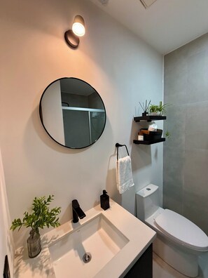 Une salle de bain avec un miroir rond, un lavabo blanc, des toilettes et un porte-serviettes.