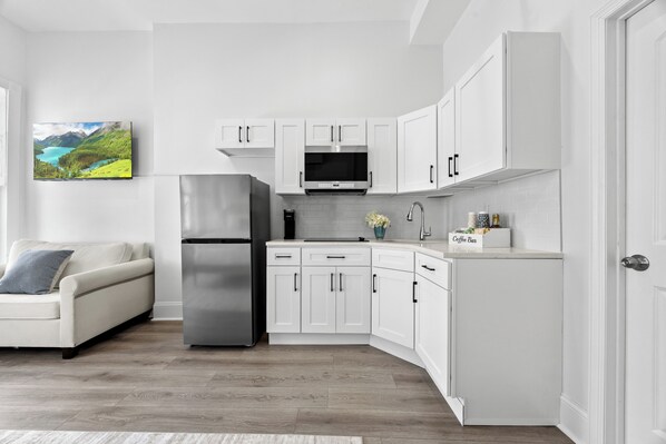 A modern kitchen with white cabinetry, a stainless steel refrigerator, and a flat-screen TV mounted above the counter.