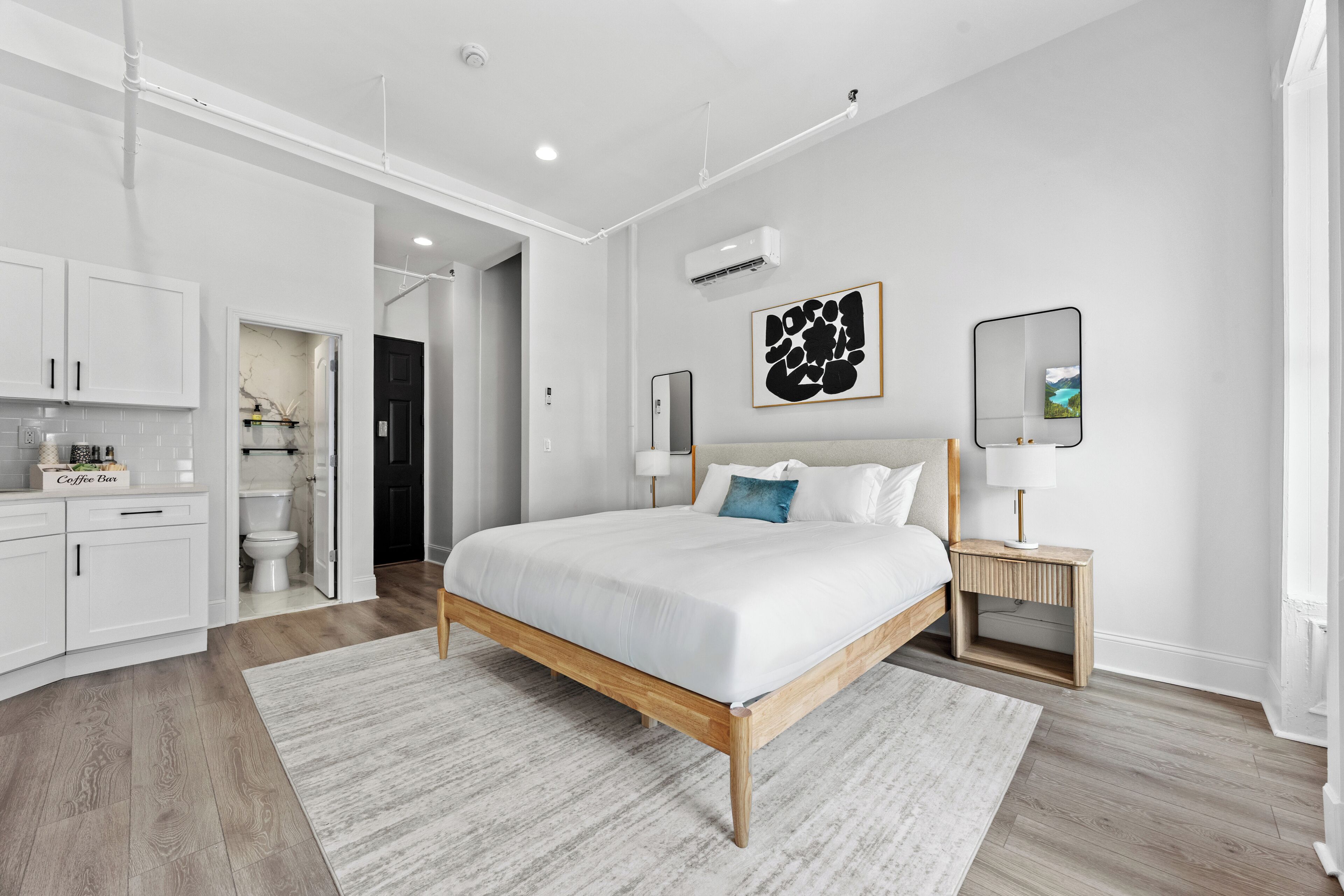 A modern bedroom with a large bed, bedside tables, a coffee bar, and a bathroom.