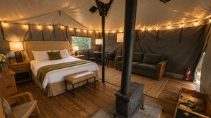 A tented accommodation with a bed, seating area, and a wood-burning stove.