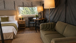 A tented room with a bed, a sofa, a table with a lamp, and a small plant.