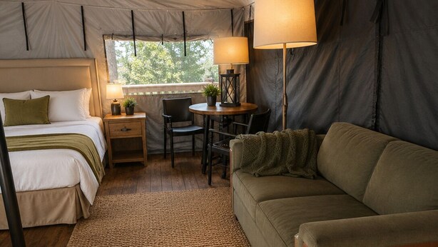 Una habitación con tienda de campaña, una cama, un sofá, una mesa con lámpara y una planta pequeña.