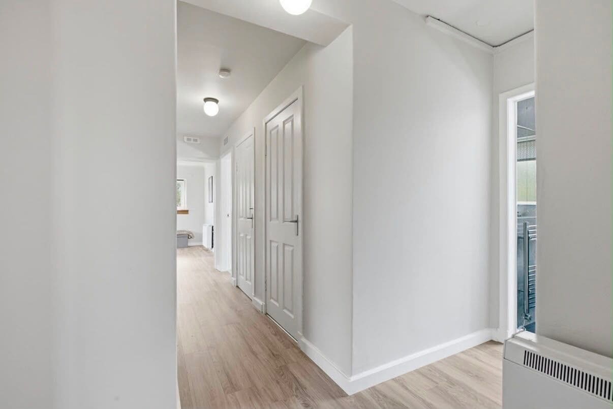 A hallway with a white door, a vent, and a window.