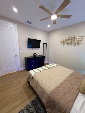 A bedroom with a bed, a dresser, a television, a ceiling fan, and a wall art piece. - La Dolce Vita | 2BR Home, Workspace & Parking in Ybor City (Tampa)