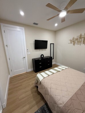 Ein Schlafzimmer mit einem Bett, einem Schminktisch, einem Fernseher, einem Deckenventilator und einer Tür.