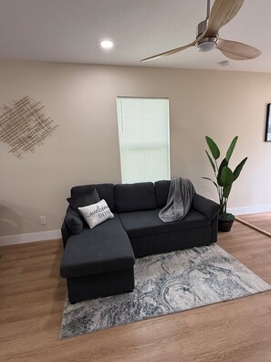 A modern living room with a sectional sofa, a ceiling fan, a potted plant, and a patterned rug. - La Dolce Vita | 2BR Home, Workspace & Parking in Ybor City (Tampa)