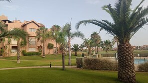A residential area with a large building, palm trees, a well-maintained lawn, and a swimming pool. - Apartment Espana On Mar Menor Golf Resort (Torre Pacheco)
