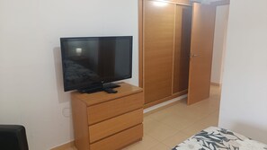 Une pièce avec un téléviseur posé sur un meuble en bois, une armoire avec une porte et un sol carrelé.