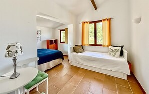 Ein Zimmer mit einem Bett, einem Sofa, einem Tisch mit einer Lampe und einem Fenster mit Vorhängen.