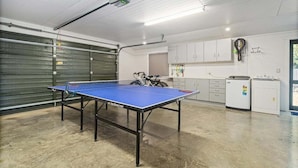 Un tavolo da ping pong in una stanza con un portone da garage, armadi e una bicicletta.