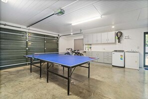 A ping pong table in a room with a garage door, cabinets, and a bicycle. - La Casa Escondida (Whitianga)