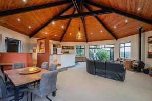 A spacious living area with a high ceiling, a fireplace, and a dining area with a table and chairs. - La Casa Escondida (Whitianga)