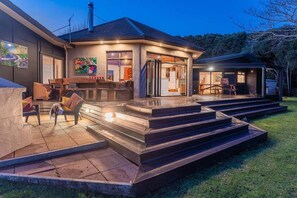 A modern house with a covered patio, outdoor seating, and a staircase leading to the entrance. - La Casa Escondida (Whitianga)