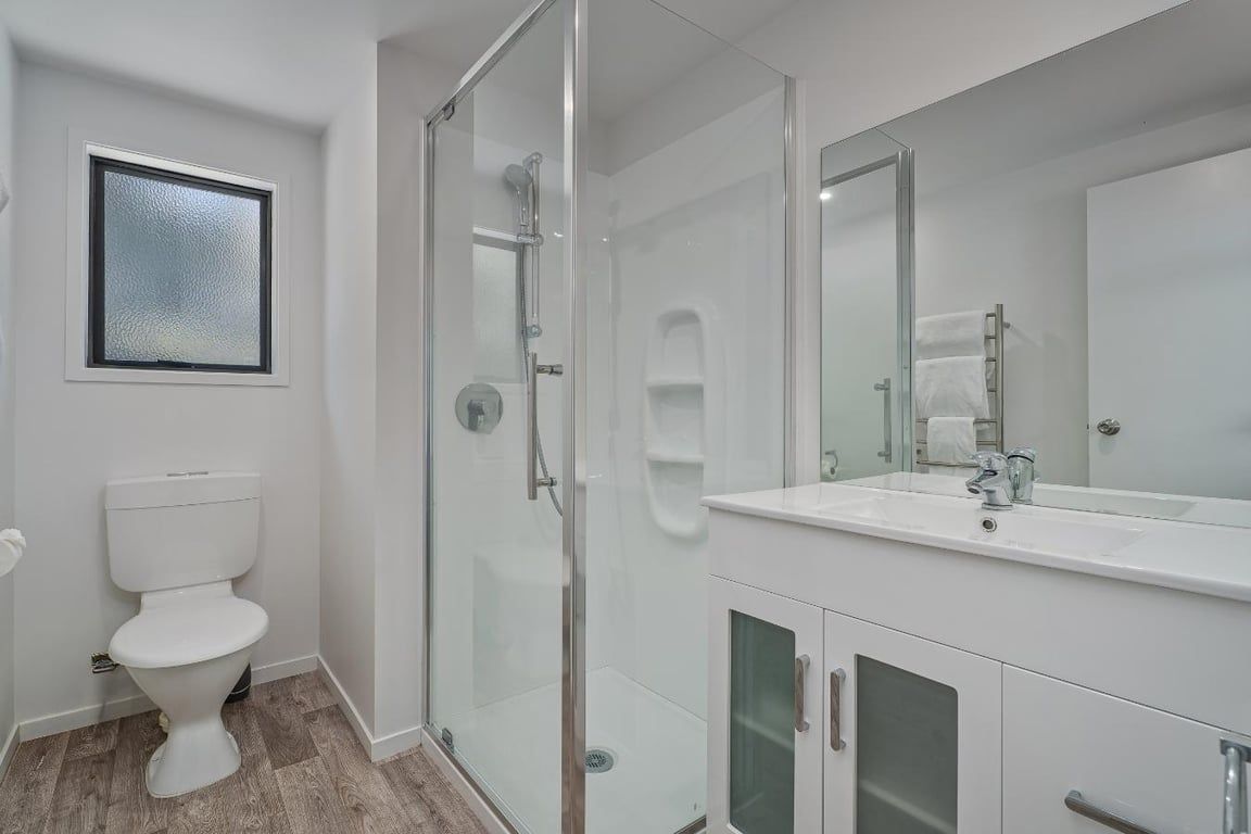 A modern bathroom with a glass-enclosed shower, a white toilet, and a vanity with a mirror.