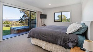 Una camera da letto con un letto grande, una televisione e una finestra vista giardino e colline.