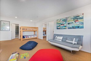 A room with bunk beds, a sofa, and a wall with abstract art. - La Casa Escondida (Whitianga)