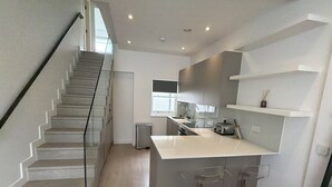 Una cocina moderna con una isla central, taburetes de bar, una escalera y un ventanal que proporciona luz natural.