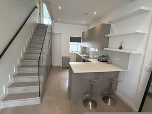 Eine moderne Küche mit einer zentralen Kochinsel, Barhocker, einer Treppe und einem Fenster für natürliches Licht.