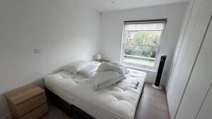 Un dormitorio con cama, mesita de noche, lámpara y ventana.