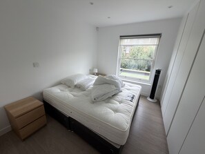 Ein Schlafzimmer mit Bett, Nachttisch, Lampe und Fenster.