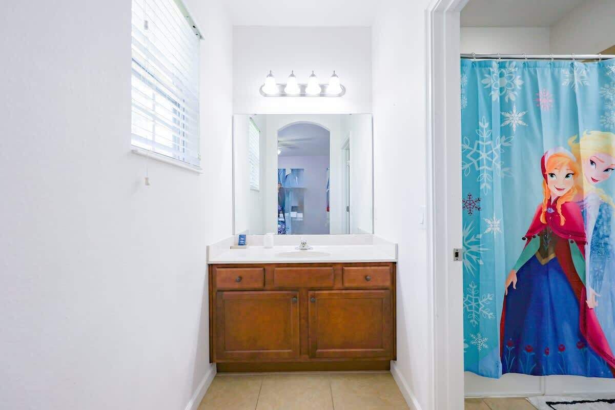 A bathroom with a vanity, a mirror, and a shower curtain with a Frozen movie character design.