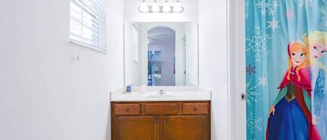 A bathroom with a vanity, a mirror, and a shower curtain with a Frozen movie character design.
