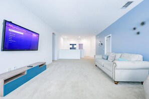 Een moderne woonkamer met een flatscreen televisie aan de wand, een witte bank en een blauwe accentmuur.