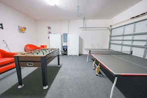 A room with a foosball table, a ping pong table, a red sofa, and a white refrigerator. - Solterra Resort Pool House 6BR/Sleeps 12 (Davenport)