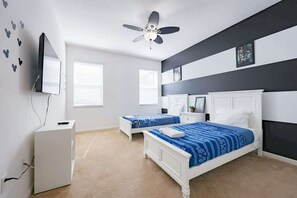 Une chambre avec deux lits, un ventilateur de plafond, une télévision et une commode.