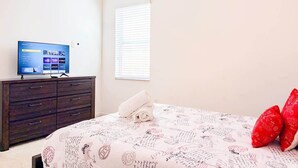 Une chambre à coucher avec un lit, un téléviseur posé sur une commode et une fenêtre avec des stores.