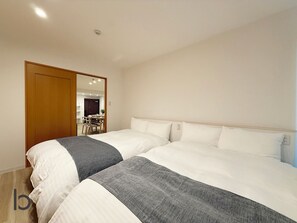 Un dormitorio con dos camas, una puerta de madera y una zona de comedor visible a través de una puerta abierta.
